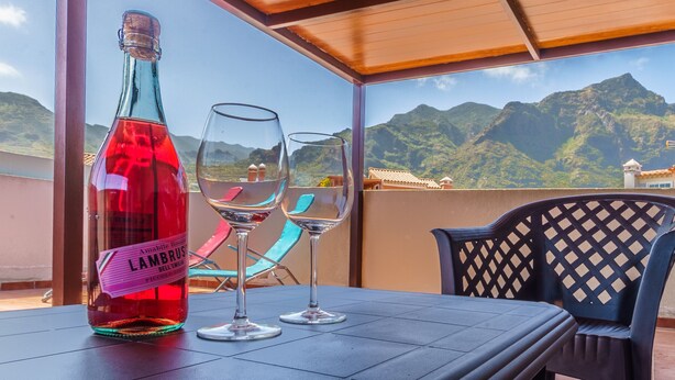 Una mesa con una botella de vino y dos copas en un balcón con vistas a montañas.