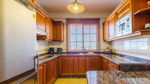 Una cocina con armarios de madera, encimera de granito, microondas integrado y una ventana con persianas.