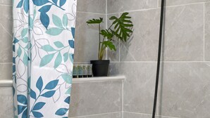 A bathroom with a shower curtain featuring a leaf pattern, a potted plant on a shelf, and tiled walls. - Impeccable 1-bed Apartment in London (London)