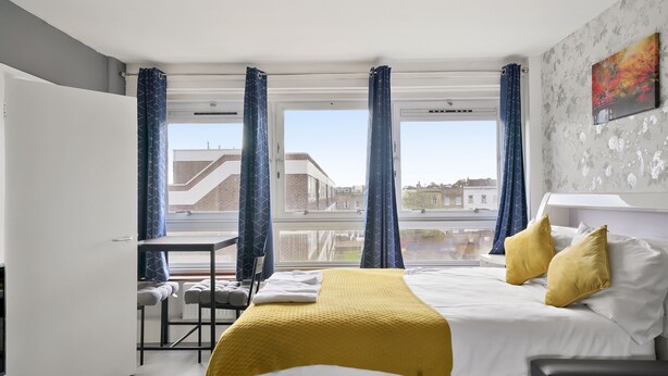 A modern hotel room with a bed, a desk, and a view of the city. - Impeccable 1-bed Apartment in London (London)