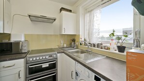 A compact kitchen with a microwave, stove, oven, and washing machine. A window with a view of the city is visible. - Impeccable 1-bed Apartment in London (London)