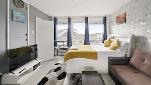 A modern hotel room with a bed, sofa, TV, and a view of buildings. - Impeccable 1-bed Apartment in London (London)