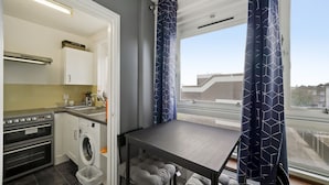 A compact kitchen with a washing machine, a table, and a window with curtains. - Impeccable 1-bed Apartment in London (London)