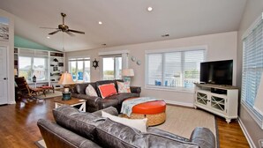 A spacious living room with a large leather sofa, a television, and a ceiling fan. - Surf N Dolphin, Oceanview House in Emerald Isle, NC! (Emerald Isle)