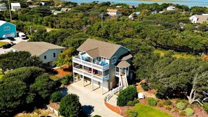 A two-story house with a balcony, surrounded by lush greenery and a view of the water. - Surf N Dolphin, Oceanview House in Emerald Isle, NC! (Emerald Isle)