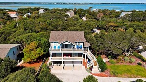 A two-story house with a balcony, surrounded by dense greenery and a view of the ocean. - Surf N Dolphin, Oceanview House in Emerald Isle, NC! (Emerald Isle)