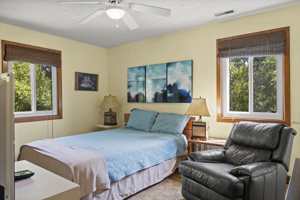 A bedroom with a bed, a chair, a nightstand, a lamp, and a painting on the wall.