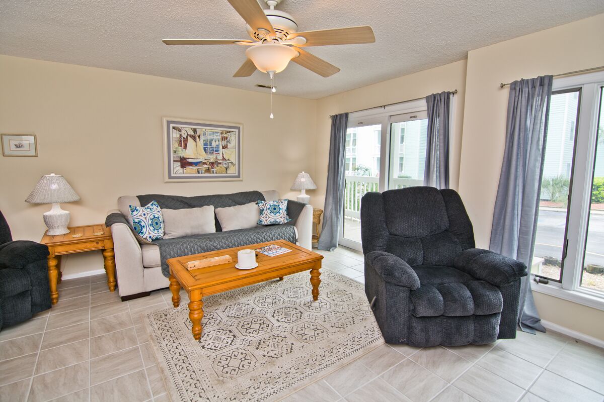 A living room with a sofa, armchair, coffee table, and a ceiling fan.