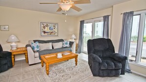 A living room with a sofa, armchair, coffee table, and a ceiling fan. - Pebble Beach E-102, Oceanview Condo in Emerald Isle, NC! (Emerald Isle)