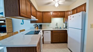 A kitchen with wooden cabinets, a white refrigerator, a dishwasher, and a ceiling fan. - Pebble Beach E-102, Oceanview Condo in Emerald Isle, NC! (Emerald Isle)