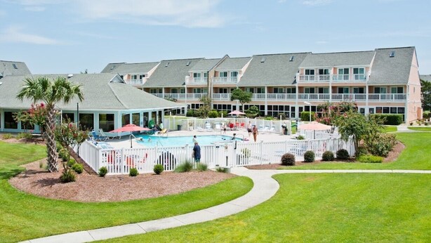 A hotel with multiple balconies, a swimming pool, and a well-maintained lawn. - Pebble Beach E-102, Oceanview Condo in Emerald Isle, NC! (Emerald Isle)