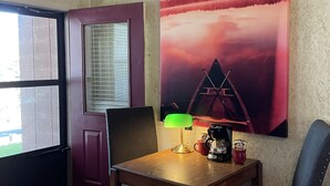 A room with a wooden table, two chairs, a lamp, a coffee maker, and a large painting of a sunset. - Mountain Harbor Queen Guest Room on Lake Ouachita by RedAwning (Mount Ida)