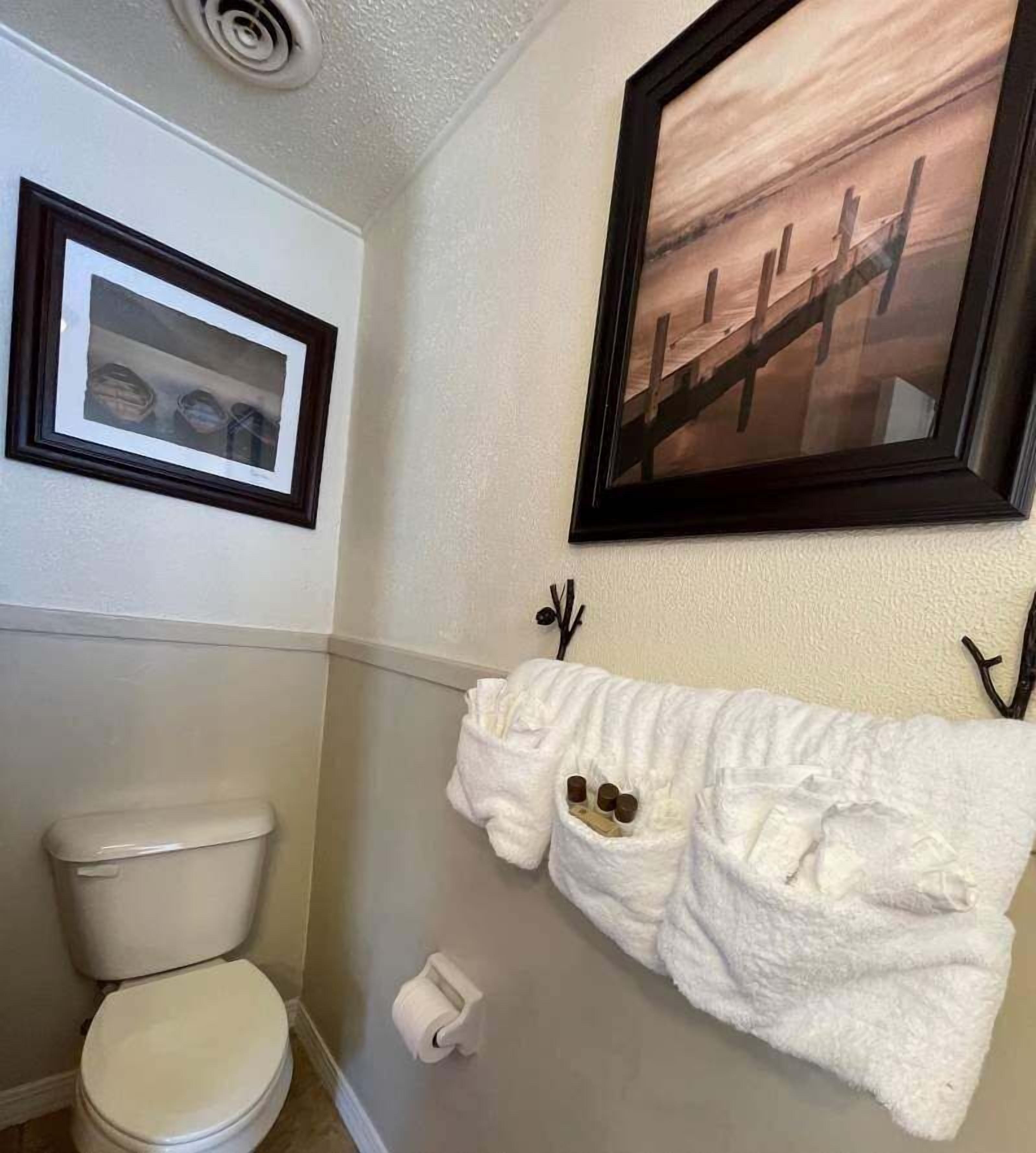 A bathroom with a toilet, a towel rack with a towel, and two framed pictures on the wall.