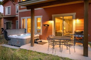 Een terras met een jacuzzi, barbecue en eettafel.