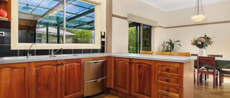 A spacious kitchen with wooden cabinets, a stainless steel dishwasher, and a large window overlooking a garden.