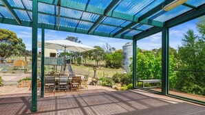An outdoor patio with wooden flooring, a table with chairs, and a covered seating area with a transparent roof. - Relaxing farmhouse & panoramic views in Glenmore  (Glenmore)