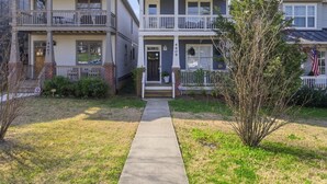 A two-story residential building with a front porch, a small front yard, and a sidewalk leading to the entrance.