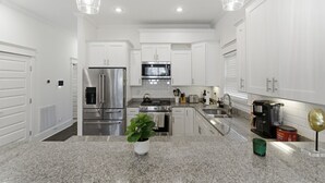 A modern kitchen with white cabinetry, stainless steel appliances, granite countertops, and pendant lighting.