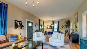 A modern living room with a sofa, two white armchairs, a coffee table, and a dining area with a table and chairs.