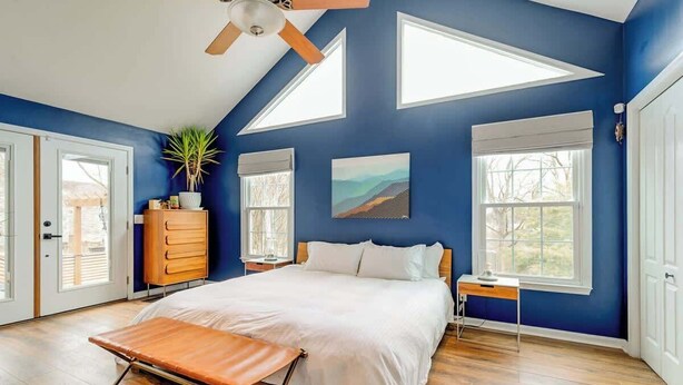 A bedroom with a bed, a desk, a ceiling fan, and a window.