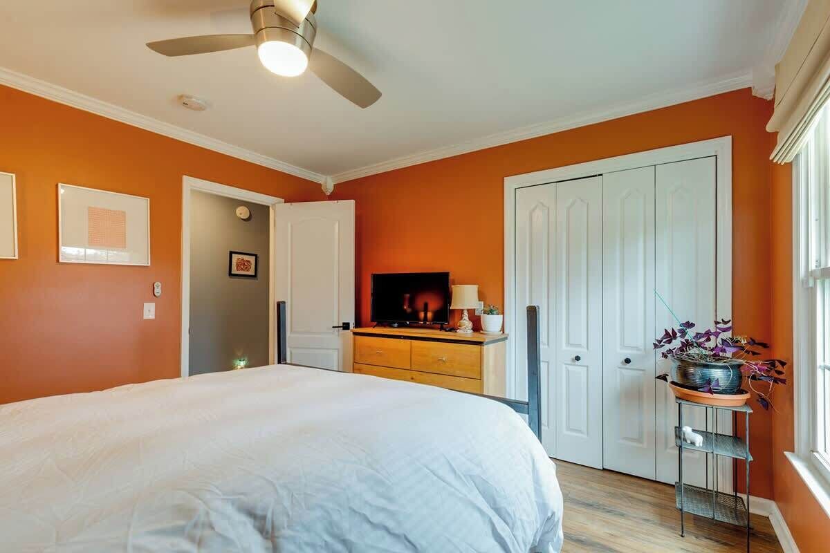 Une chambre à coucher avec un lit, un ventilateur de plafond, une télévision, une commode et une fenêtre avec une plante.