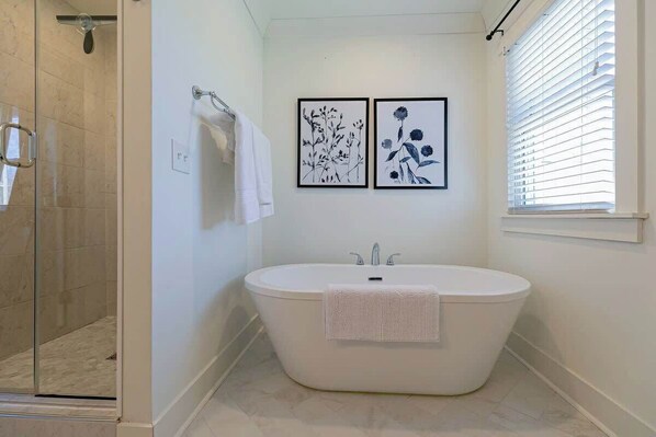 Un baño moderno con una bañera independiente, un box de ducha de vidrio y dos impresiones botánicas enmarcadas en la pared.