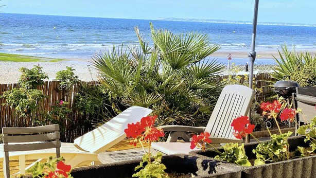 Eine Terrasse direkt am Strand mit Liegestühlen, einem weißen Sonnenschirm und Blick auf das Meer.