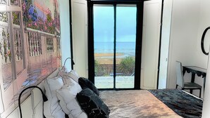 Ein Schlafzimmer mit einem großen Bett, Blick auf den Strand und einem Wandgemälde.