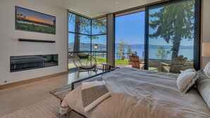 A bedroom with a large bed, a fireplace, and a view of a lake and mountains. - Peace of Tahoe - Lakefront - TLUXP (Carnelian Bay)