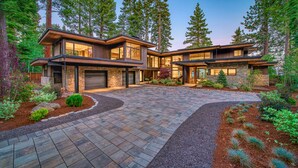 A modern two-story house with a stone facade, large windows, and a driveway leading to a garage. - Peace of Tahoe - Lakefront - TLUXP (Carnelian Bay)