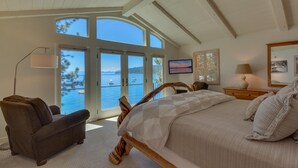 Un dormitorio con una cama grande, una silla, un televisor y vista al agua.