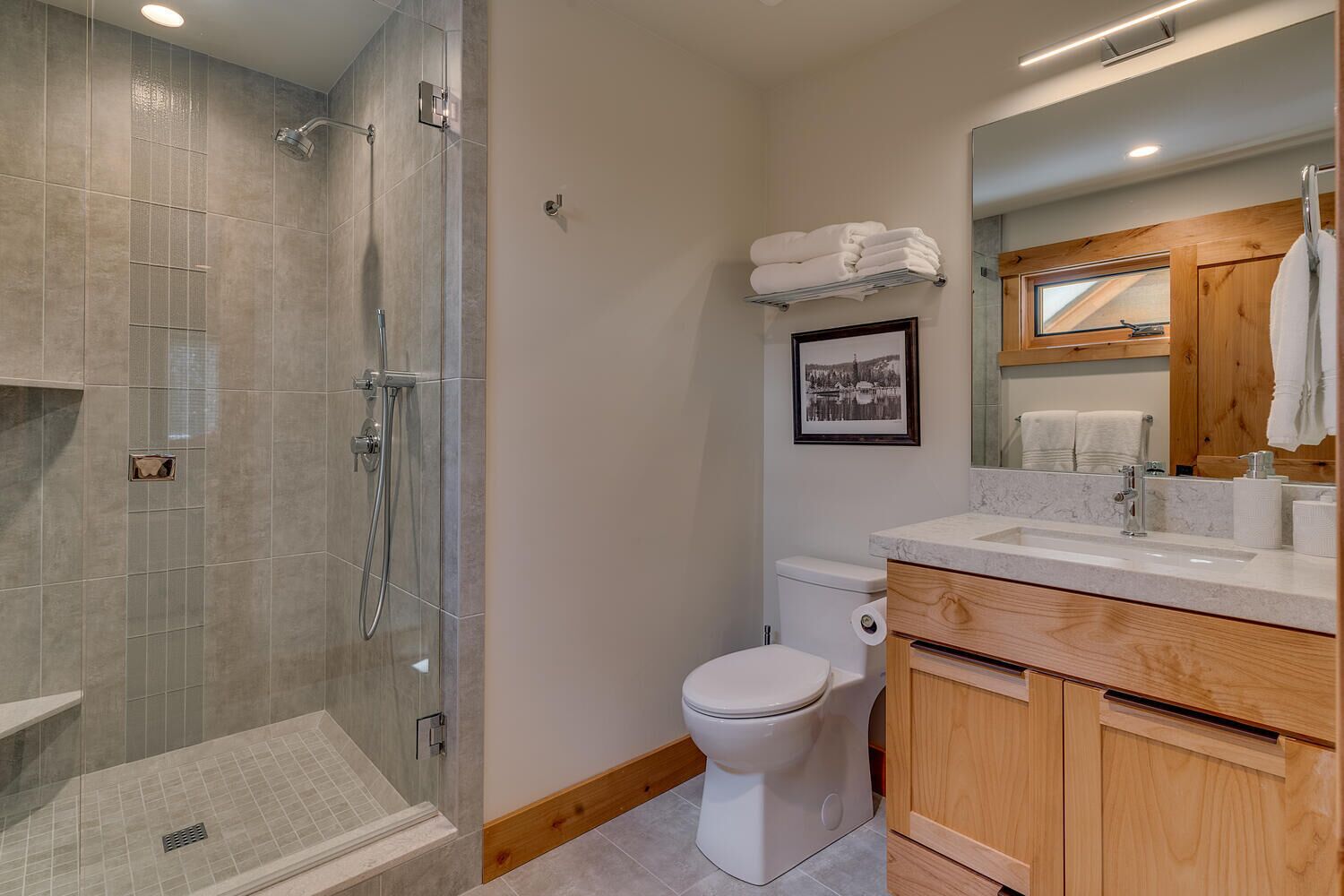 Un baño moderno con ducha de vidrio, inodoro y tocador con espejo.