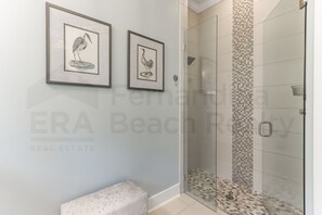 A bathroom with a glass shower, tiled walls, and two framed bird illustrations on the wall.