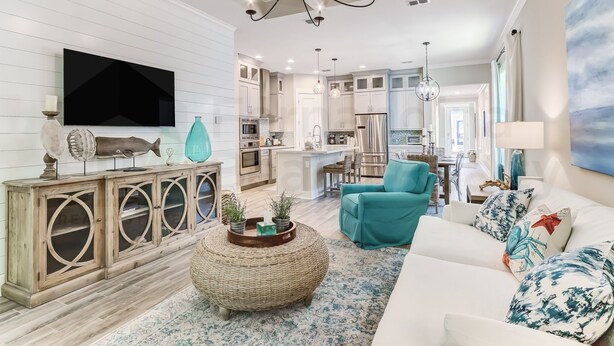 A modern living room with a large TV, a teal armchair, and a white sofa with patterned cushions.