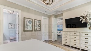 A bedroom with a large bed, a TV, and a dresser. There are framed pictures on the wall and a bench in the corner.