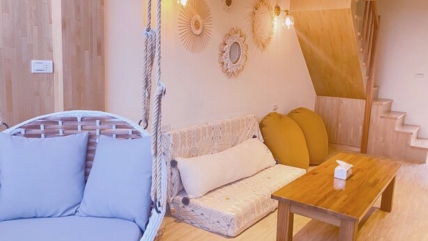 Una habitación acogedora con una silla colgante, un sofá con cojines, una mesa de madera y adornos en la pared.