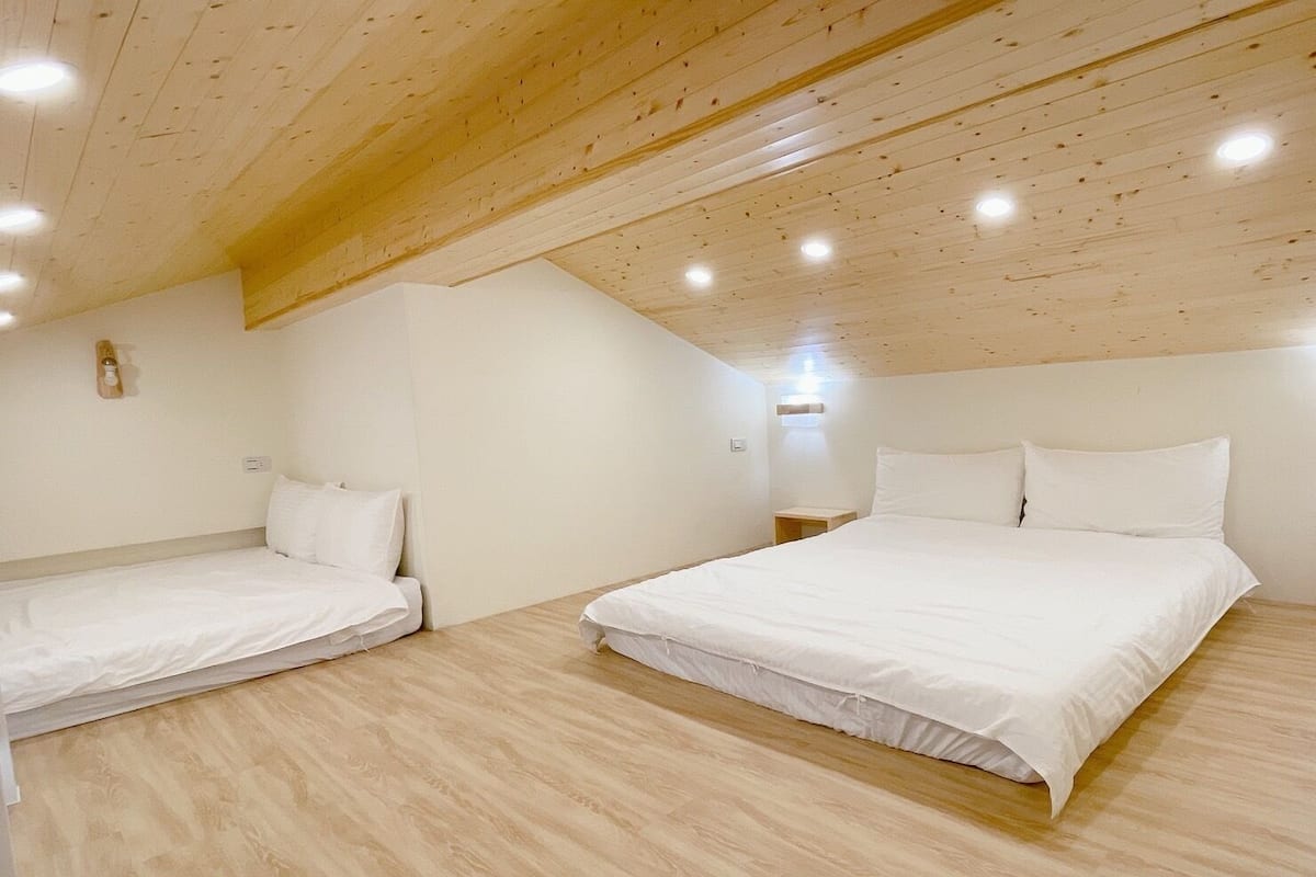 A bedroom with two beds, wooden ceiling beams, and recessed lighting.