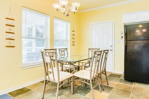 A dining area with a glass table surrounded by six chairs, a black refrigerator, and a window with blinds. - Dog Friendly, Private Beachside Home in Pirates Beach w/ Covered Deck (Galveston)
