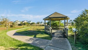 A gazebo with a wooden deck, surrounded by a grassy area and a curved pathway. - Dog Friendly, Private Beachside Home in Pirates Beach w/ Covered Deck (Galveston)
