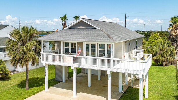 A single-story house with a covered porch and a small deck, surrounded by palm trees and a clear sky. - Dog Friendly, Private Beachside Home in Pirates Beach w/ Covered Deck (Galveston)