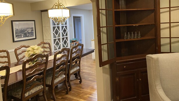 Un espace repas avec une longue table en bois, des chaises décorées et un lustre.