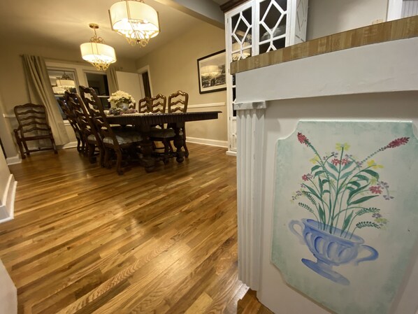 A dining area with a wooden table and chairs, a chandelier, and a decorative painting on the wall.