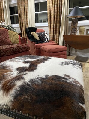 A room with a patterned sofa, a red armchair, a wooden side table, and a lamp.