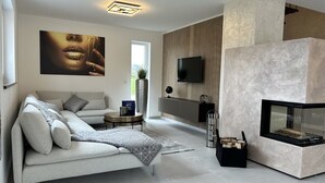 Ein modernes Wohnzimmer mit einer Couch, einem Kamin, einem Fernseher und einem großen Fenster.
