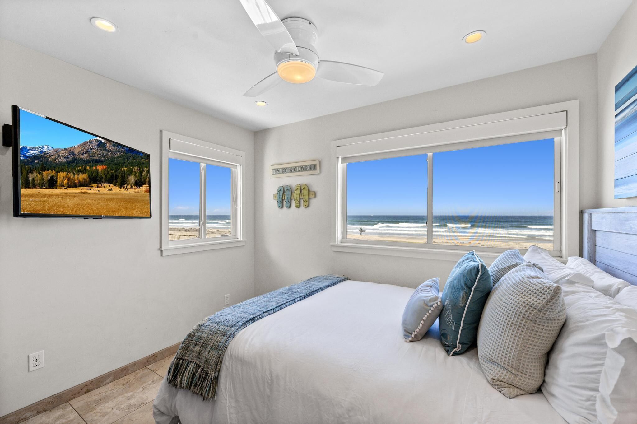 A bedroom with a bed, a ceiling fan, and a TV displaying a mountain landscape.