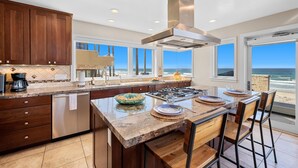 A modern kitchen with a large island, wooden cabinets, and a view of the ocean. - Cielo Mar | 4BR Oceanfront Escape + Rooftop (San Diego)