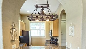 A kitchen with an island, two bar stools, a chandelier, and wooden cabinets.