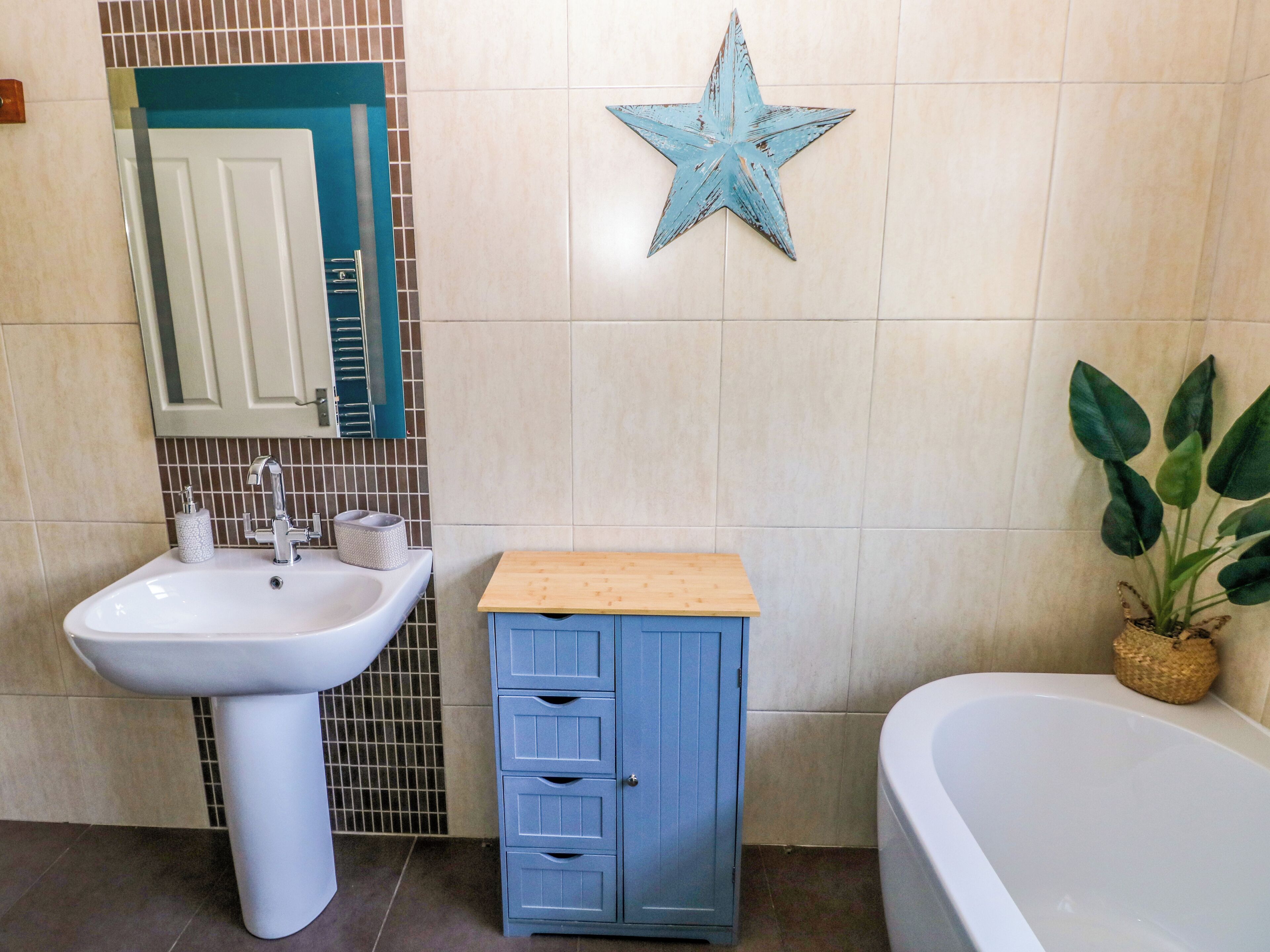 A bathroom with a white sink, a blue cabinet, a star decoration, and a bathtub.