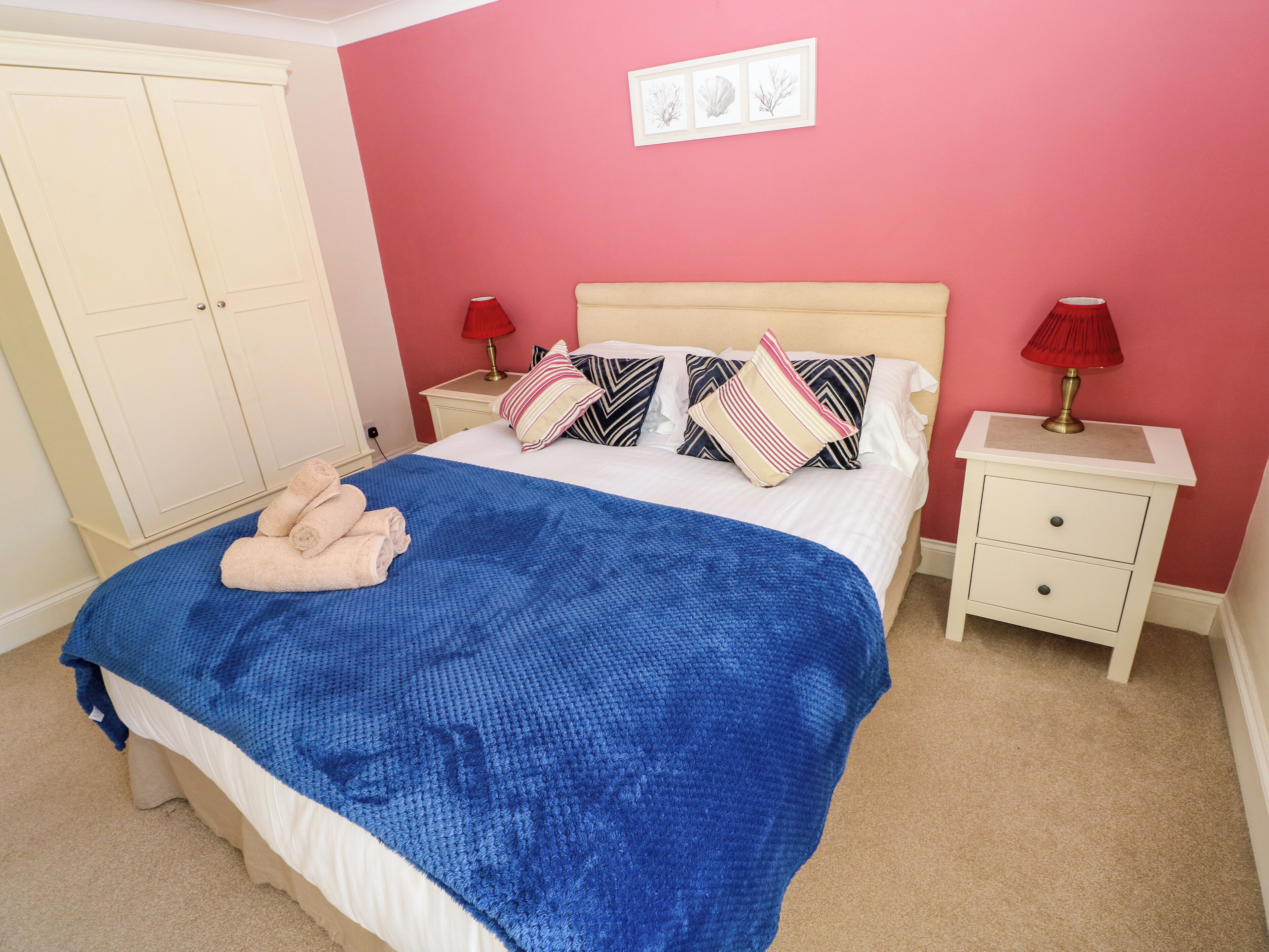 A bedroom with a bed, two bedside tables, a wardrobe, and a wall with three framed pictures.
