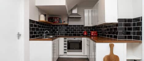 Compact kitchen with oven, wooden cutting board, and white cabinetry.